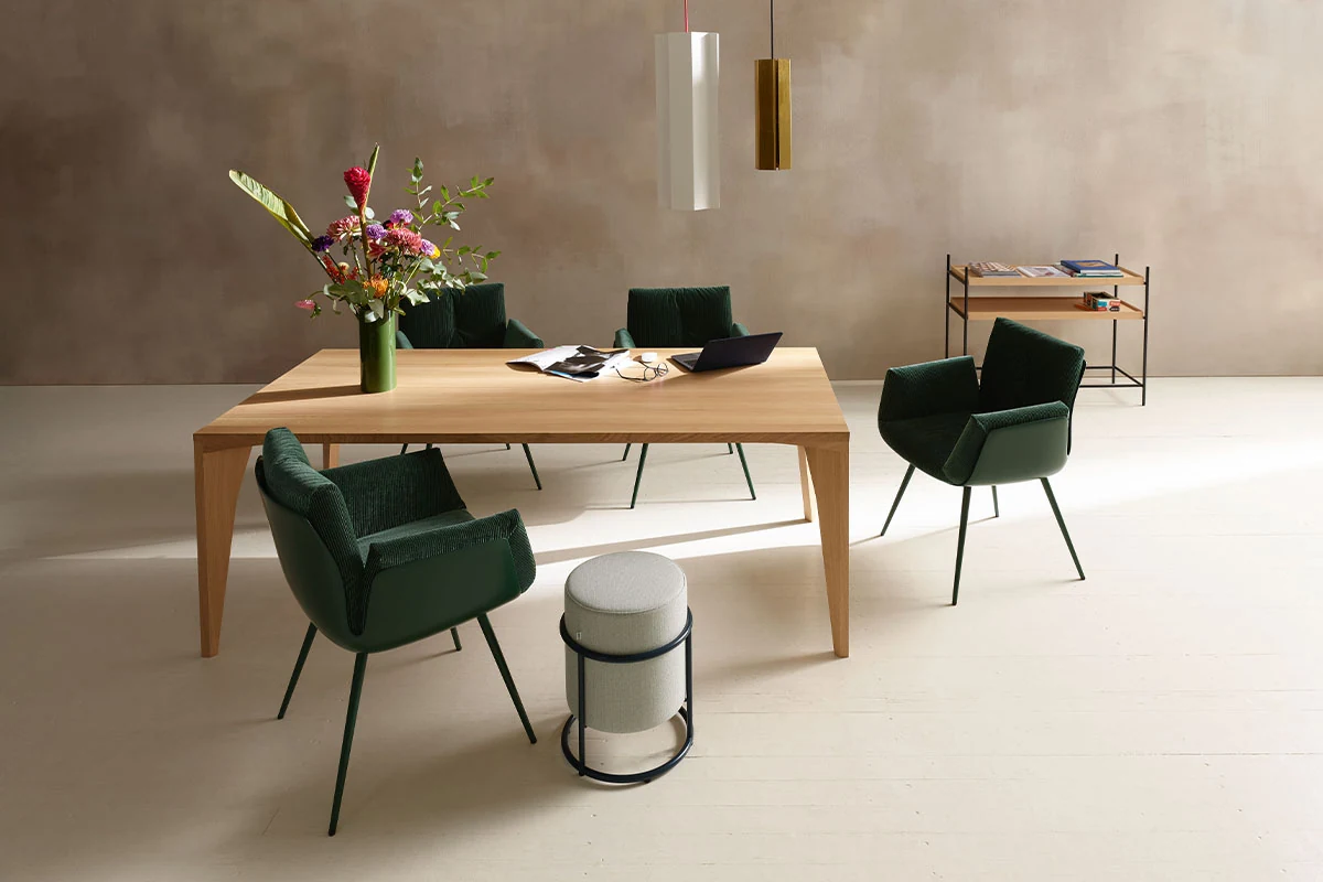 Zwei grün bezogene COR Alvo Stühle mit filigranen schwarzen Gestellen an einem Holztisch