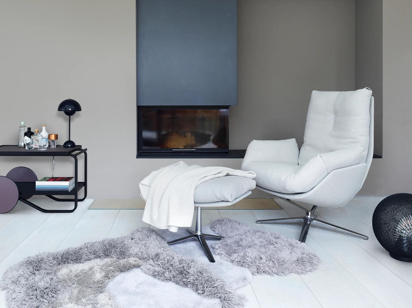 Heller COR Cordia Lounge mit passendem Hocker und zurückgeneigter Rückenlehne vor einem Kamin