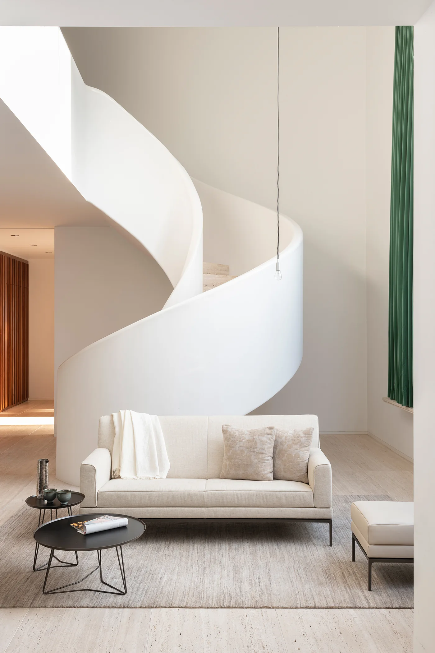 Helles JORI Glove Pure Sofa mit schlankem dunklem Gestell vor einer geschwungenen Treppe