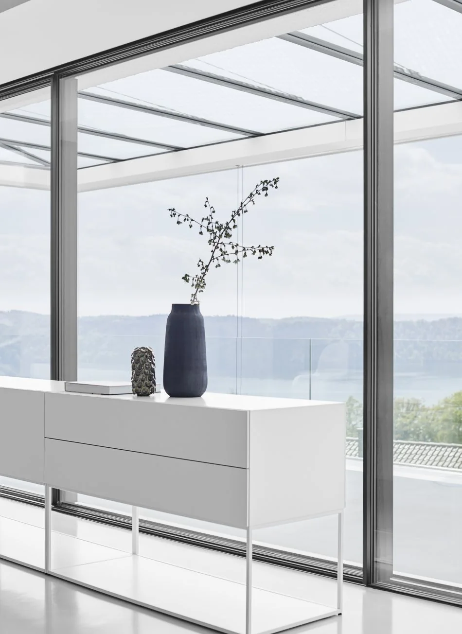 Weißes ALEA-Sideboard auf schlankem Gestell vor einer Glasfront