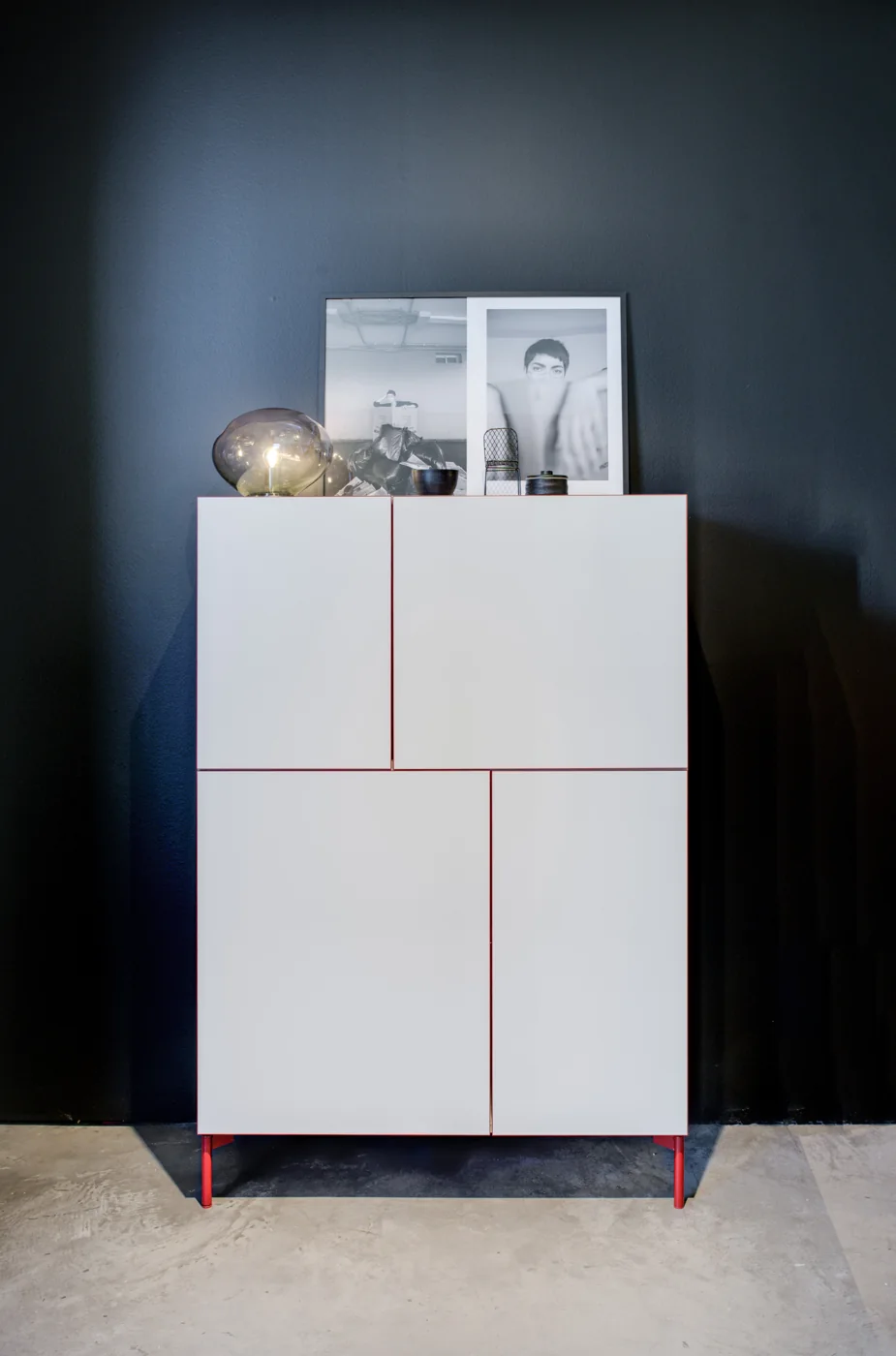 Weißes CASE-Highboard mit feinen farbigen Fugen und schlanken Füßen vor einer dunklen Wand