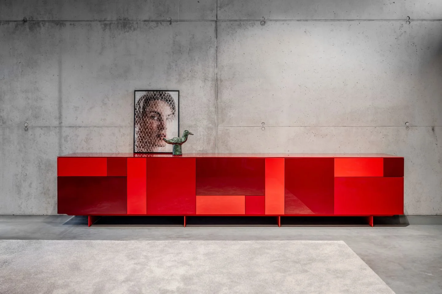 Rotes Kettnaker SOMA 2.0-Sideboard mit unterschiedlich angeordneten Blenden vor einer Betonwand