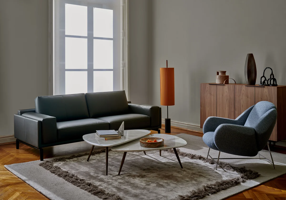 Dunkles Leolux Bellice Sofa in einer Wohnsituation mit blauem Sessel und runden Tischen
