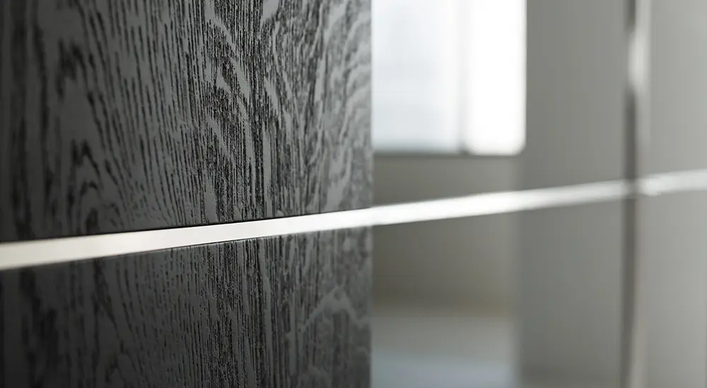 Detail eines VARUS Schranks mit dunkler Holzmaserung und schmalem Edelstahlkreuz